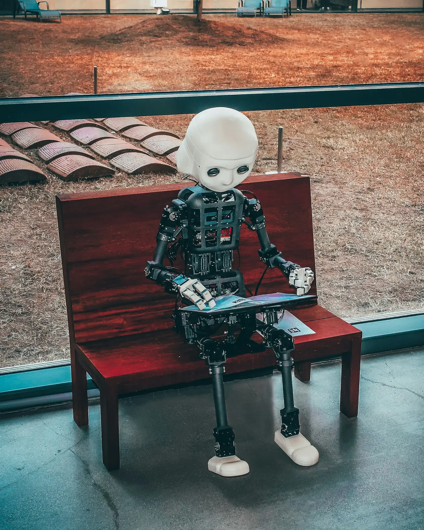 Humanoid robot seated on a bench working on a small laptop