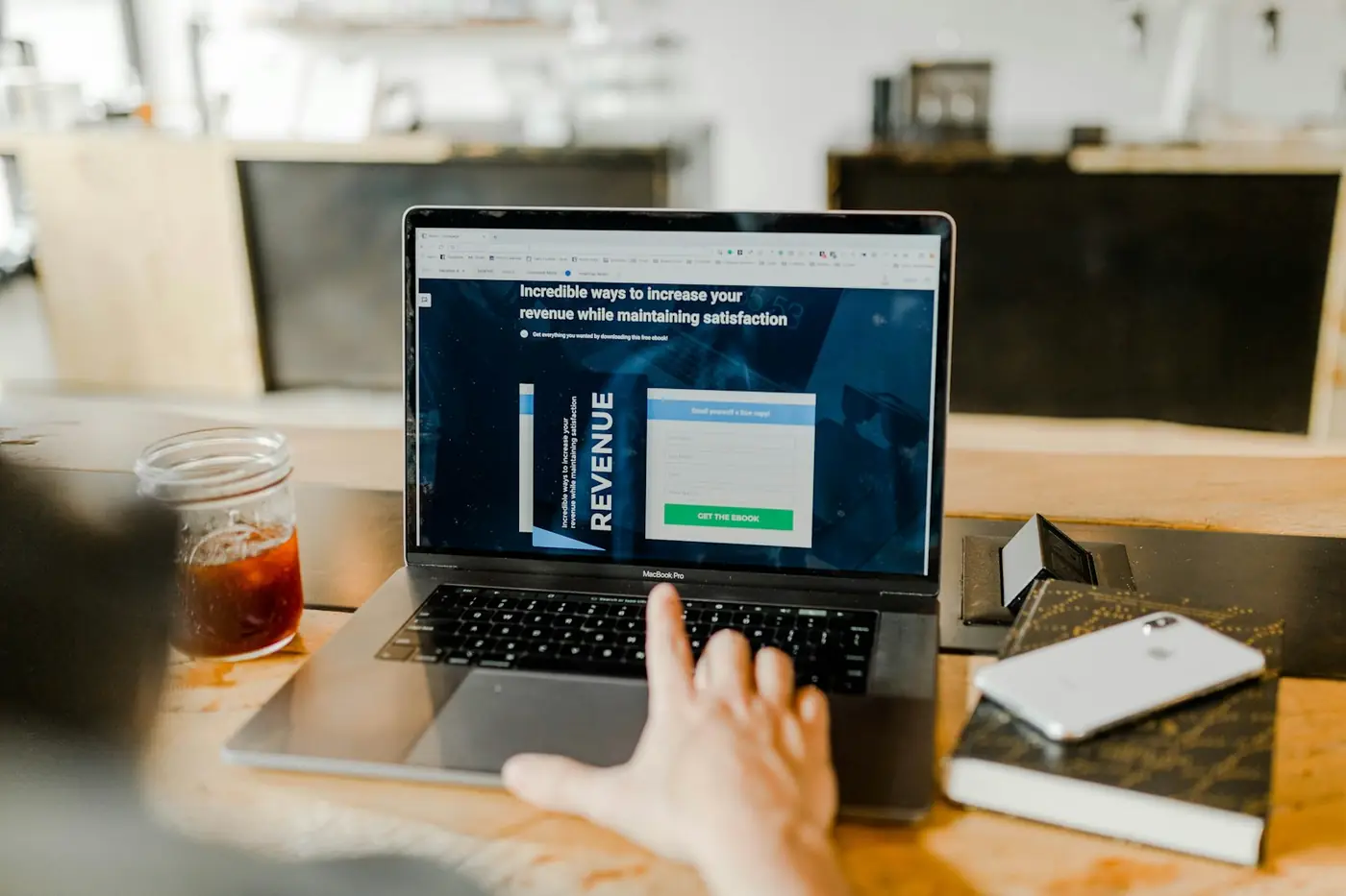 Hand scrolling a conversion optimization page on a laptop in a bright workspace