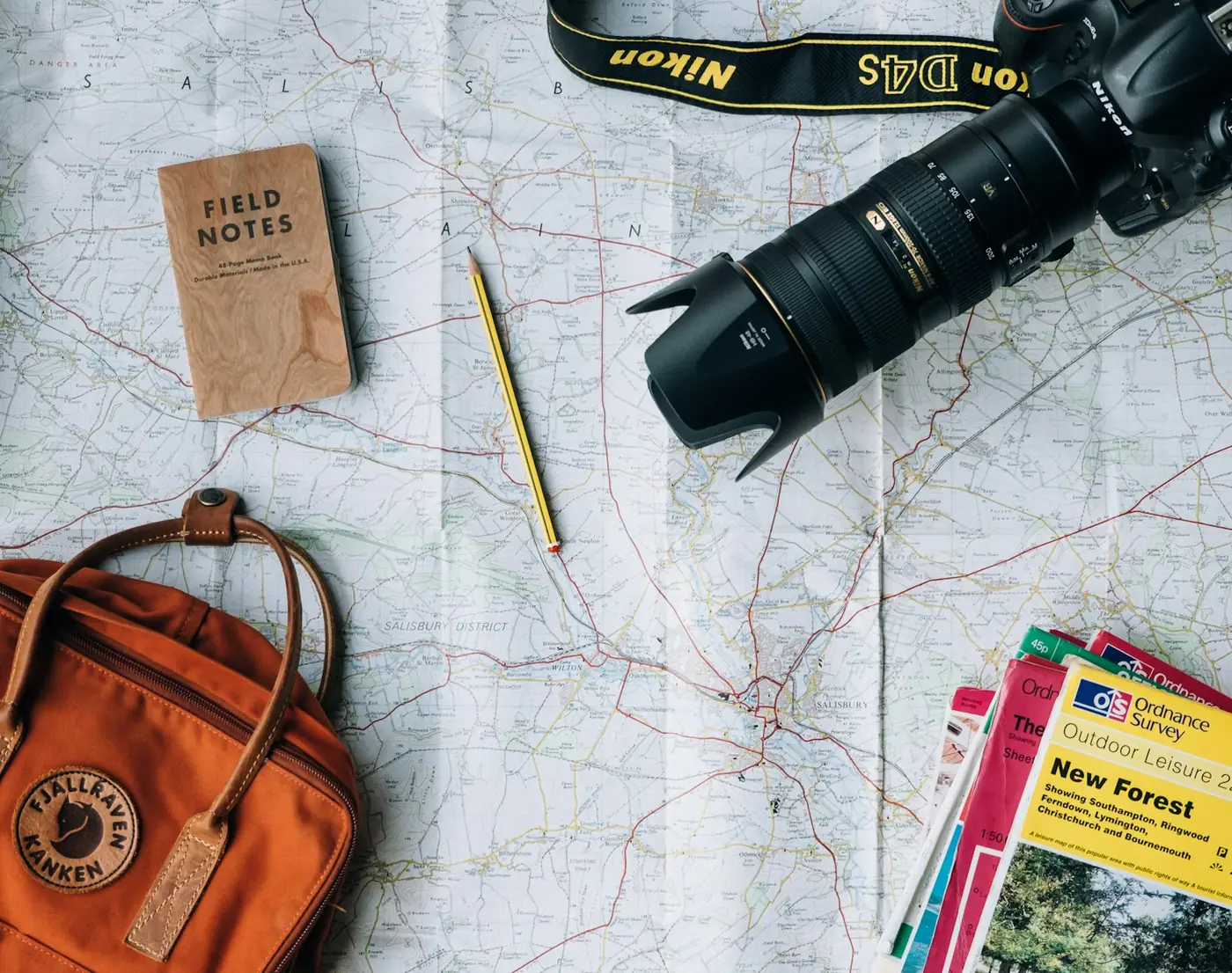 Trail map, backpack, camera, and field notebook laid out for an outdoor trip